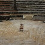 störtebeker festspiele - Lone wooden chair on an amphitheater stage surrounded by trees.